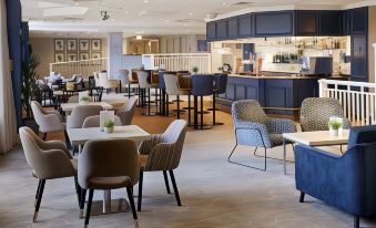 a modern restaurant with various dining tables , chairs , and booths , as well as a kitchen area at Coldra Court Hotel by Celtic Manor