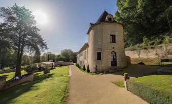 a large stone building with a round tower is surrounded by a lush green lawn and trees at Hôtel Saint-Martin - la Maison Younan