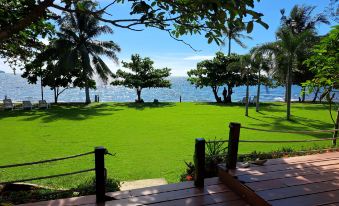 a view of a grassy area with palm trees and a body of water in the background at Lomtalay Resort Trat