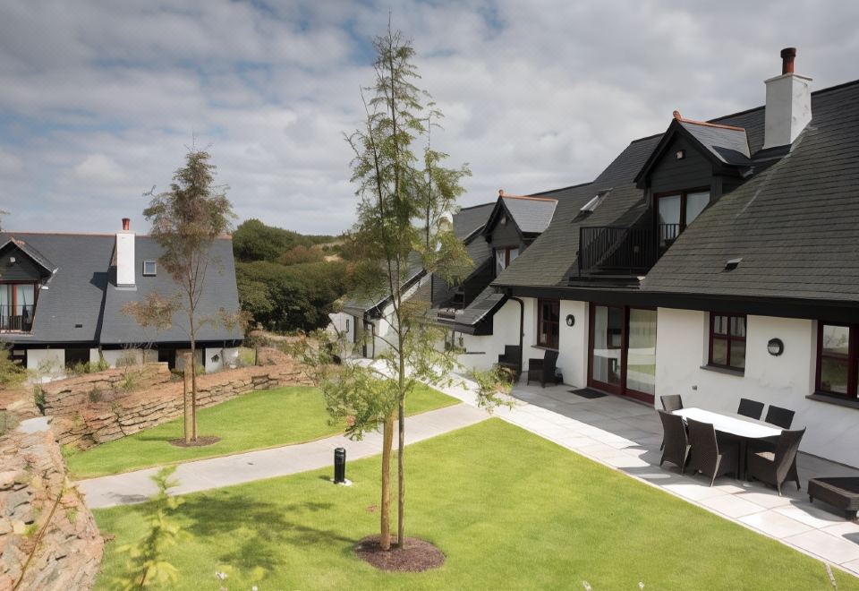 a large , modern house with a green lawn and a tree in the front yard at Hustyns Resort Cornwall