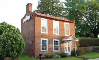 a red brick house with a chimney and white trim is surrounded by green grass and trees at Lafayette Inn