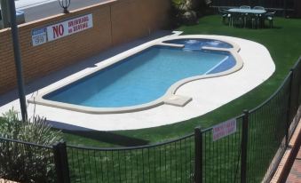 a small backyard with a swimming pool surrounded by grass , and a fence surrounding the area at Carnegie Motor Inn