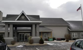 a modern building with a gray roof , surrounded by snow and trees , under a cloudy sky at Country Inn & Suites by Radisson, Kalamazoo, MI