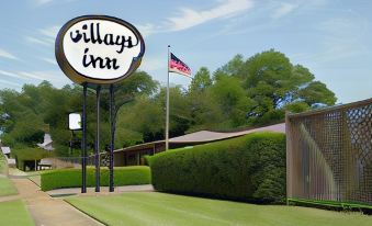 a large sign for the village inn is displayed in front of a building with bushes and trees at Village Inn