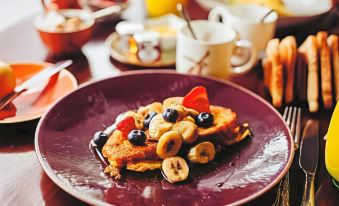 a plate of pancakes topped with bananas , blueberries , and strawberries sits on a dining table at Banchory Lodge Hotel