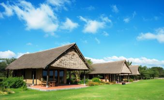 a grassy field with several wooden houses , some of which are covered in thatched roof roofing at Sweetwaters Serena Camp