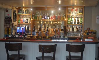 a well - stocked bar with various bottles and glasses , as well as several chairs in the background at The Queen Victoria