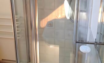 a bathroom with a clear glass shower door , a white towel on the floor , and a shower head attached to the wall at Chalk and Cheese