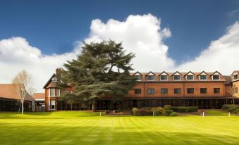 a large , modern building with a green lawn and tall trees in front of it at Mercure Hull Grange Park Hotel