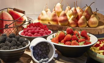 a dining table with a variety of fresh fruits , including raspberries , blueberries , and pears , arranged in bowls at Steigenberger Airport Hotel Berlin