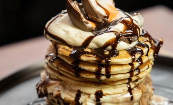 a stack of pancakes topped with whipped cream and chocolate sauce , sitting on a table at Arthouse Hotel