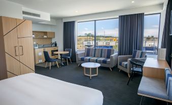 a hotel room with a bed , couch , dining table , chairs , and a view of the outdoors at Alpha Hotel Eastern Creek