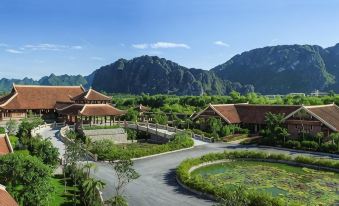 a picturesque mountain village with a thatched - roof building , surrounded by lush greenery and mountains in the background at Emeralda Resort Ninh Binh