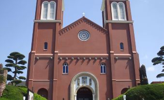a red brick church with a clock tower and two tall steeple stands in front of it at Nagasaki Nisshokan