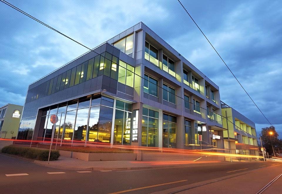 a modern building with large windows and a red circle logo is reflected in the glass at Hotel 115