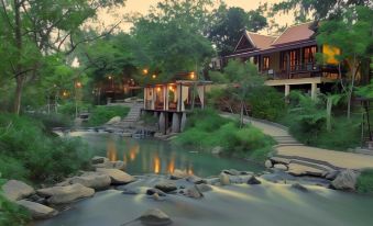 a serene scene of a wooden house surrounded by lush greenery , with a stream flowing nearby at Zantiis Ndol Villas