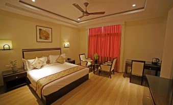 a large bed with a white and gold comforter is in the middle of a room with wooden floors and red curtains at Hotel Royal Inn