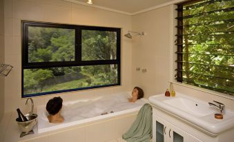 two women are relaxing in a large bathtub with a view of trees outside the window at Whispering Valley Cottage Retreat