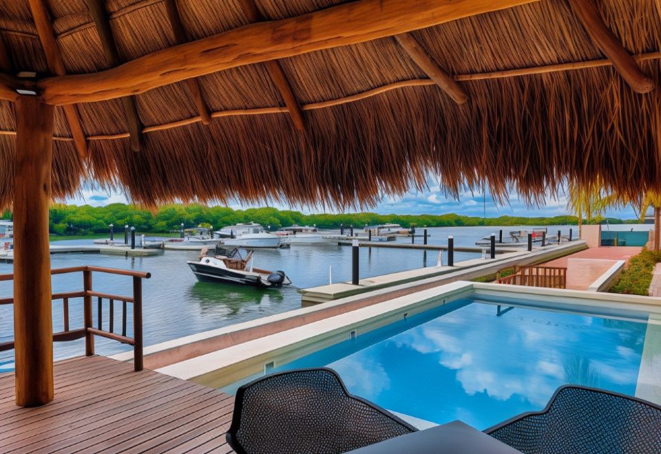 a wooden deck with a thatched roof overlooks a swimming pool and boats on the water at Villas Grand Marina Kinuh