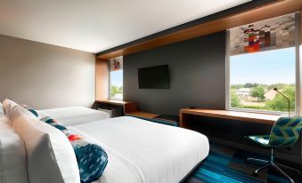 a hotel room with two beds , a window offering a view of the city , and a large screen tv at Aloft Hillsboro-Beaverton
