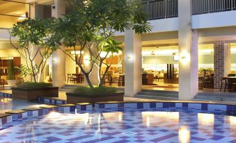 a hotel with a large outdoor pool surrounded by chairs and tables , as well as a dining area nearby at Bueno Colombo Hotel Yogyakarta