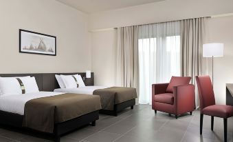 a hotel room with two beds , a red armchair , and a framed picture on the wall at Inn Naples Airport