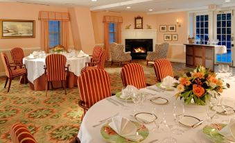 a dining room with a fireplace and several tables set for a meal , including round tables with white tablecloths and red chairs at The Inn at Montchanin Village