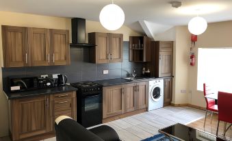 a modern kitchen with wooden cabinets , black appliances , and white tiles , along with a living room area at Green Apartments