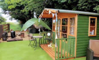 a small wooden house with a green roof and a table and chairs on the deck at Glamping with Llamas