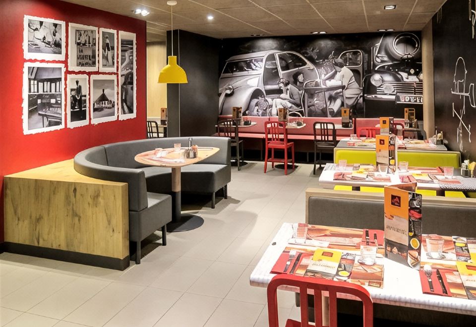 a restaurant with red tables and chairs , gray booths , and a black and white photo on the wall at Ibis Lyon Villefranche-Sur-Saône