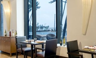 a restaurant with wooden tables and chairs , a large window , and a view of the ocean at Novotel Mumbai Juhu Beach