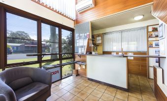 a modern office reception area with wooden walls , large windows , and a white counter , along with a couch and table at Iluka Motel