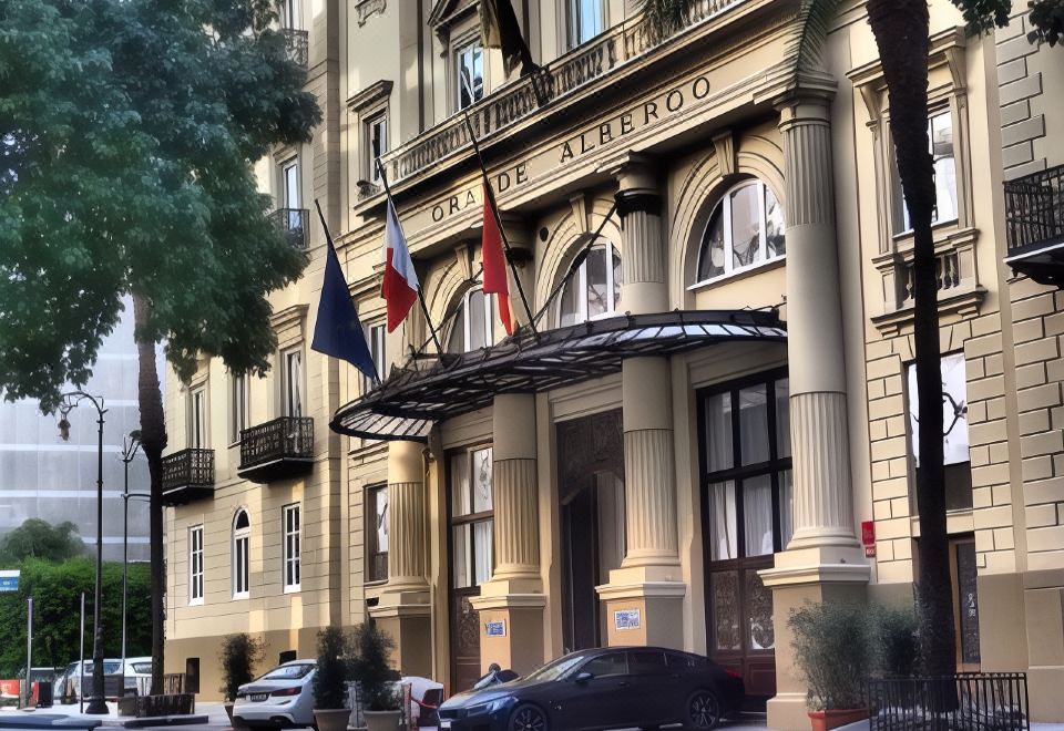 a large building with multiple flags flying on the front , and cars parked in front of it at Grand Hotel Et des Palmes