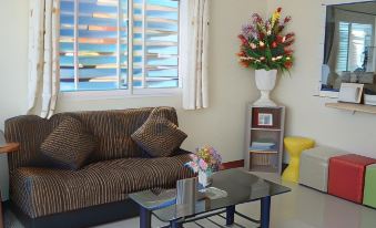 a cozy living room with a brown couch , a glass coffee table , and a vase of flowers on the window sill at Tulip Place