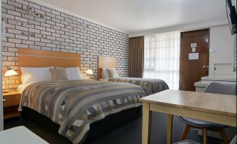 a hotel room with two beds , a desk , and a brick wall , giving it a cozy and comfortable atmosphere at The Heritage Bendigo