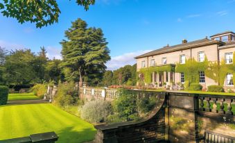a large house with a garden and stone wall is surrounded by trees and bushes at Doxford Hall Hotel and Spa
