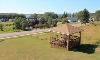 a wooden gazebo with a brown roof is situated on a grassy field , overlooking a body of water at The Fiddle and the Sea Bed and Breakfast