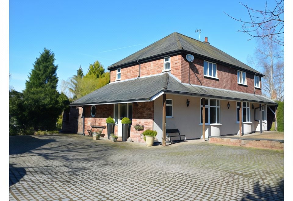 a brick house with a large driveway and trees in the background , under a clear blue sky at Laburnum Cottage Guest House