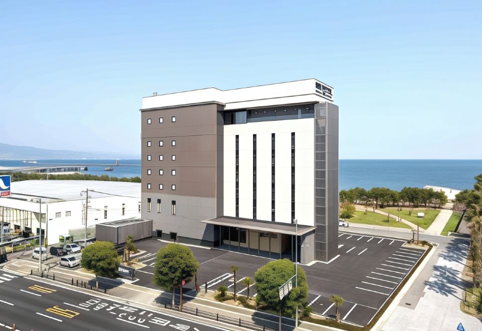 a modern building with a large parking lot in front of it , surrounded by trees and overlooking the ocean at Rex Hotel Beppu