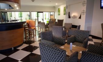 a modern lounge area with black and white checkered flooring , several chairs , tables , and potted plants at Highlander Hotel
