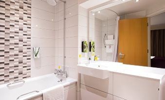 a modern bathroom with white tiled walls , a large mirror , and a bathtub filled with towels at Premier Inn Bangor (Gwynedd, North Wales)