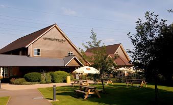 a large building with a restaurant in the middle of a grassy area with several picnic tables at Premier Inn Tewkesbury