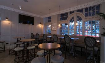 a modern bar with white walls , wooden floors , and large windows , featuring several tables and chairs arranged for dining at The Kings Head Hotel