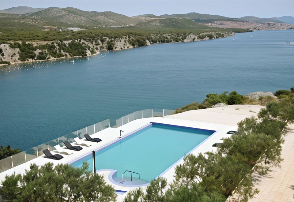 a large outdoor swimming pool surrounded by trees and mountains , with a view of the ocean in the background at Hotel Panorama