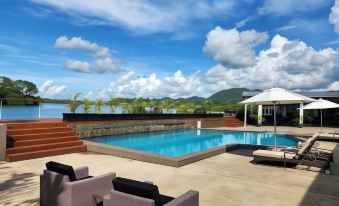 a large outdoor pool surrounded by lounge chairs and umbrellas , with a view of the ocean in the background at Novotel Suva Lami Bay