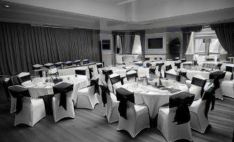 a large dining room with round tables covered in white tablecloths and black chairs adorned with bows at Waveney House Hotel