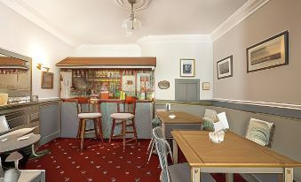 a cozy dining room with wooden tables and chairs , a red rug , and a small bar in the background at Bridgeside Guest House