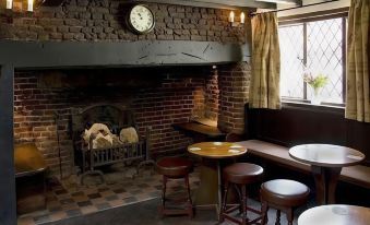 a cozy pub interior with brick walls , wooden floors , and stools around a fireplace , offering a warm atmosphere at The Brocket Arms