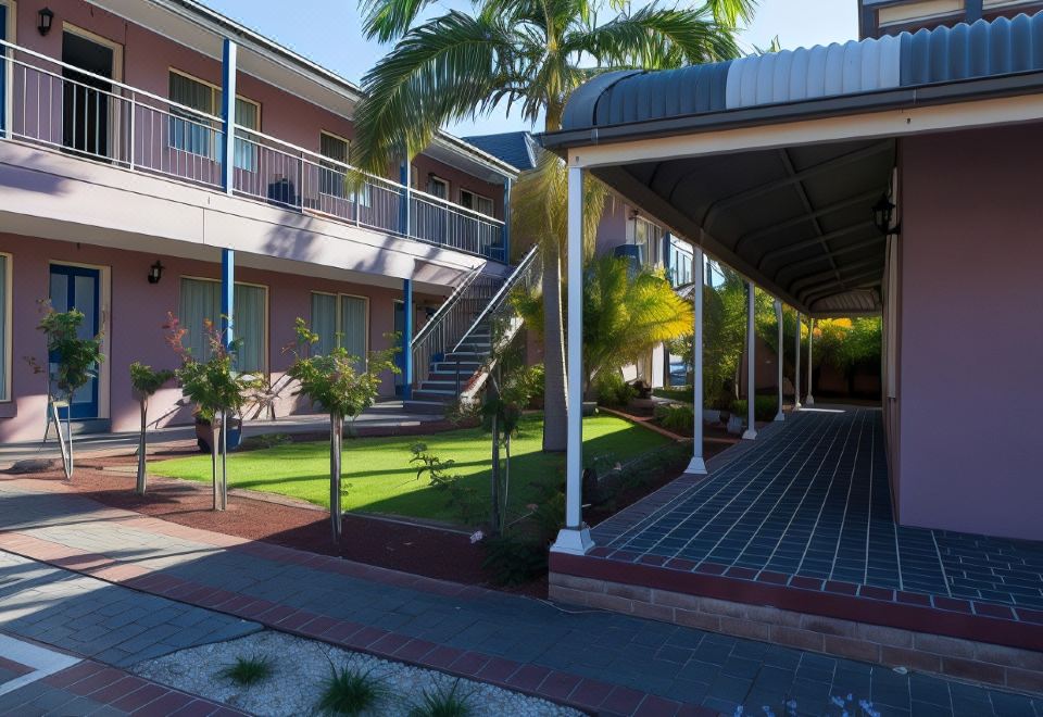 a courtyard with a building , stairs , and potted plants is surrounded by grass and palm trees at Shellharbour Village Motel