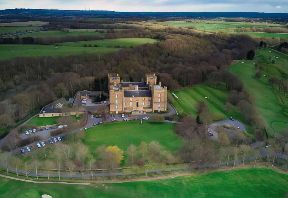 an aerial view of a castle surrounded by green fields and trees , with a road in the foreground at Lumley Castle Hotel